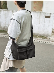 Detail view of a black nylon crossbody bag with dual front pockets and adjustable strap