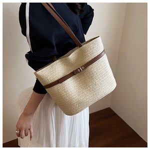Close-up of a large woven straw tote bag featuring leather straps and buckle detail