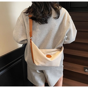 Detail of cream nylon dumpling crossbody bag with adjustable brown strap and logo patch