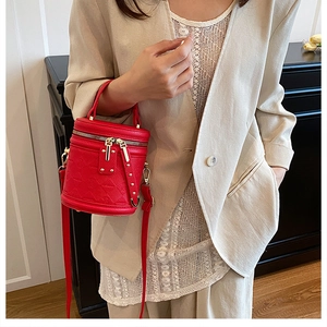 Detail of red embossed leather bucket bag with gold studs and dual zippers on a shoulder strap