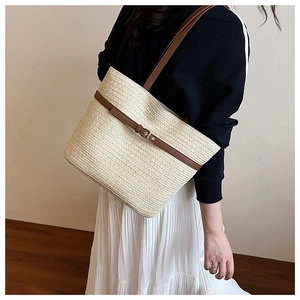 Close-up of woven straw tote bag with brown leather straps and metallic buckle detail
