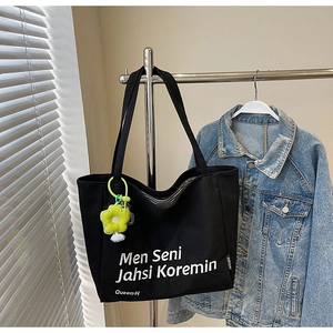 Detail of black canvas tote with white lettering, yellow flower charm and denim background