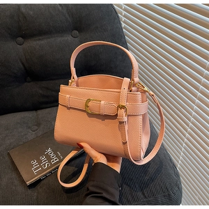 Détail du sac à main en cuir litchi rose avec boucle dorée sur un canapé chic