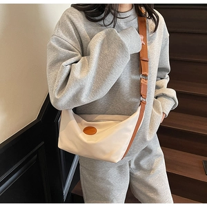 Beige nylon crescent bag with adjustable brown strap and decorative leather patch details