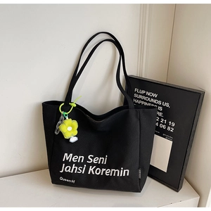 Detail of black canvas tote bag with artistic white lettering and yellow flower charm