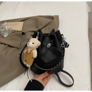 Detail of black bucket bag with pebble texture, silver chain strap and a plush bear charm