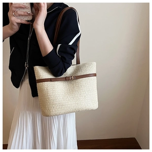 Detailed view of woven straw tote bag featuring brown leather strap and metal horseshoe buckle