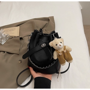 Detail of black pebbled leather bucket bag with chain strap and cute bear plush charm