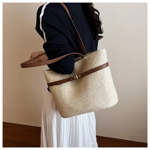 Detail view of woven straw tote bag with brown leather strap and buckle on model