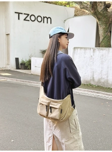 Detail of a large beige nylon crossbody bag with functional utility pockets and wide strap