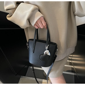 Close-up of black lychee texture bucket bag with silver heart charm on modern staircase