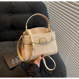Détail du sac en cuir crème avec texture litchi et bandoulière sur un canapé gris