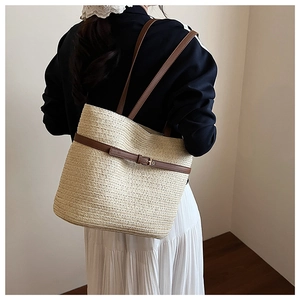 Close-up of a woven straw tote bag with brown leather straps and gold buckle detail
