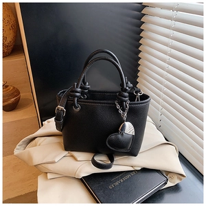 Chic black lychee grain bucket bag with heart pendant on a beige blazer background