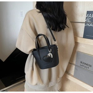 Detail of a black bucket bag with pebble leather texture and heart-shaped charm accessory