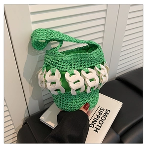 Close-up of green hand-woven straw bucket bag with white circular link decorative chain