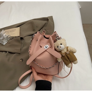 Detail of pink bucket bag with lychee texture leather, metal chain, and cute bear charm