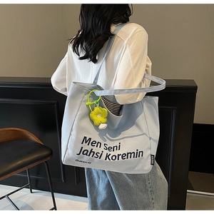 Detail view of light blue canvas tote bag with black typography and yellow flower pendant