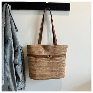 Detailed macro view of woven straw beach tote bag with brown leather buckle and strap