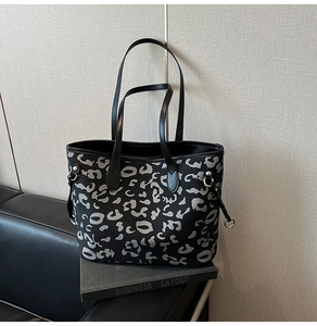 Dettaglio della borsa tote leopardata con manici in pelle nera sopra un libro