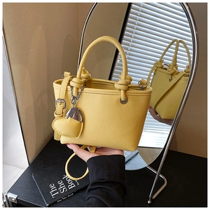 Detail of yellow lychee leather bucket bag featuring a silver chain and heart charm