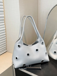 Silver metallic leather tote bag with eyelet details on a book in a minimalist setting