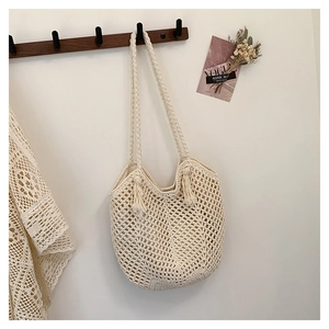 Detailed close-up of cream knit tote bag featuring fringe accents and braided shoulder strap