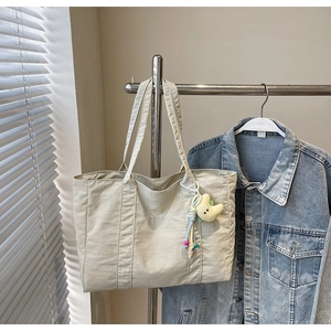 Detail view of a beige canvas tote bag with TaoCaiFu text and a star plush charm