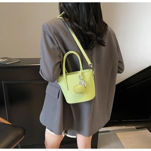 Side view of lime green lychee leather bucket bag with silver heart charm and strap
