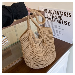 Detail of hand-woven beige straw tote bag featuring decorative tassels and a soft fabric lining