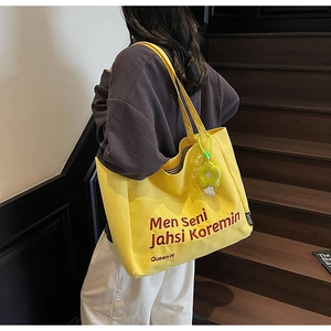 Close-up of yellow canvas tote bag with red text and sunflower charm on a model