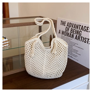 Detail of cream crochet tote bag with hollow patterns, fringe, and thick woven handles