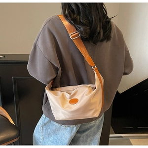Detail of champagne nylon dumpling bag with wide brown strap shown on a model