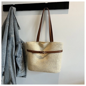 Detail of woven straw tote bag featuring brown leather shoulder straps and decorative metal buckle