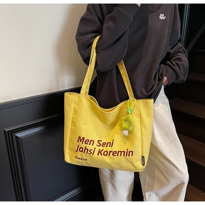 Detailed view of yellow canvas tote bag with red text and green flower charm