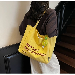 Detail of yellow canvas tote bag with brown text and a floral charm on the side