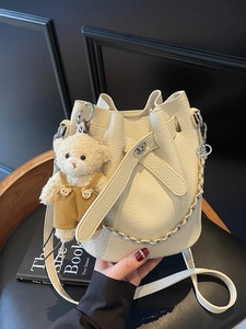 White lychee pattern bucket bag with chain strap and teddy bear charm on wooden seat