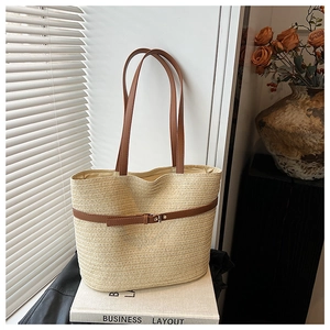 Detail of woven straw tote bag featuring brown leather straps and buckle accents