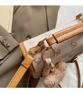 Close-up of printed cylindrical crossbody bag with gold hardware and plush bear charm