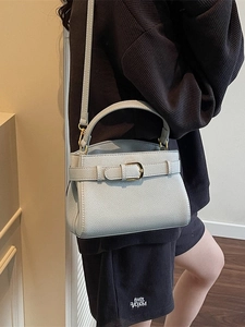 Sac à main chic en cuir bleu clair avec boucle dorée porté à l'épaule par un mannequin