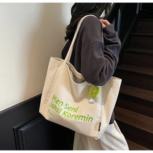 Detail of canvas tote bag with green letter embroidery and yellow flower charm