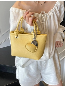 Yellow lychee leather bucket bag with knot handle and heart pendant shown on model