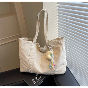 Detail of off-white nylon tote bag with TaoCai embroidery and moon pendant on leather chair
