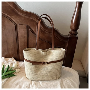 Close-up of woven straw tote bag with brown leather straps and gold buckle detail