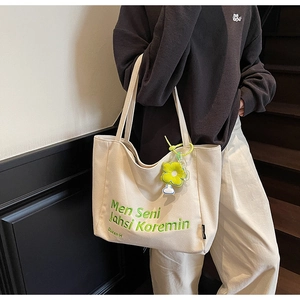 Close-up of cream canvas tote bag with green embroidery and yellow flower charm detail