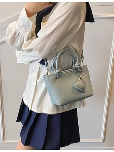 Light blue faux leather bucket bag with knot handle and heart charm shown on a model