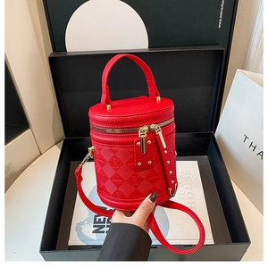 Close-up of red cylinder bucket bag with litchi grain and gold zippers in a luxury gift box