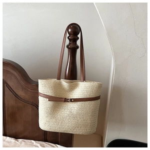 Detail of a beige woven straw tote bag featuring brown faux leather straps on a wooden post