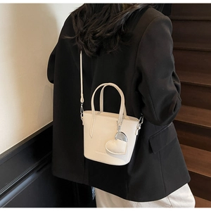 Detail of cream white bucket bag with lychee texture and heart charm on a black suit
