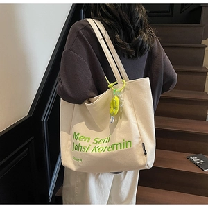 Detail of cream canvas tote with green embroidery and matching charm on a shoulder strap